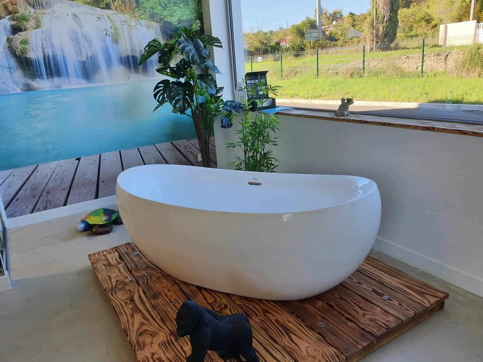 Baignoire îlot exposée dans le showroom, devant une fresque de cascade