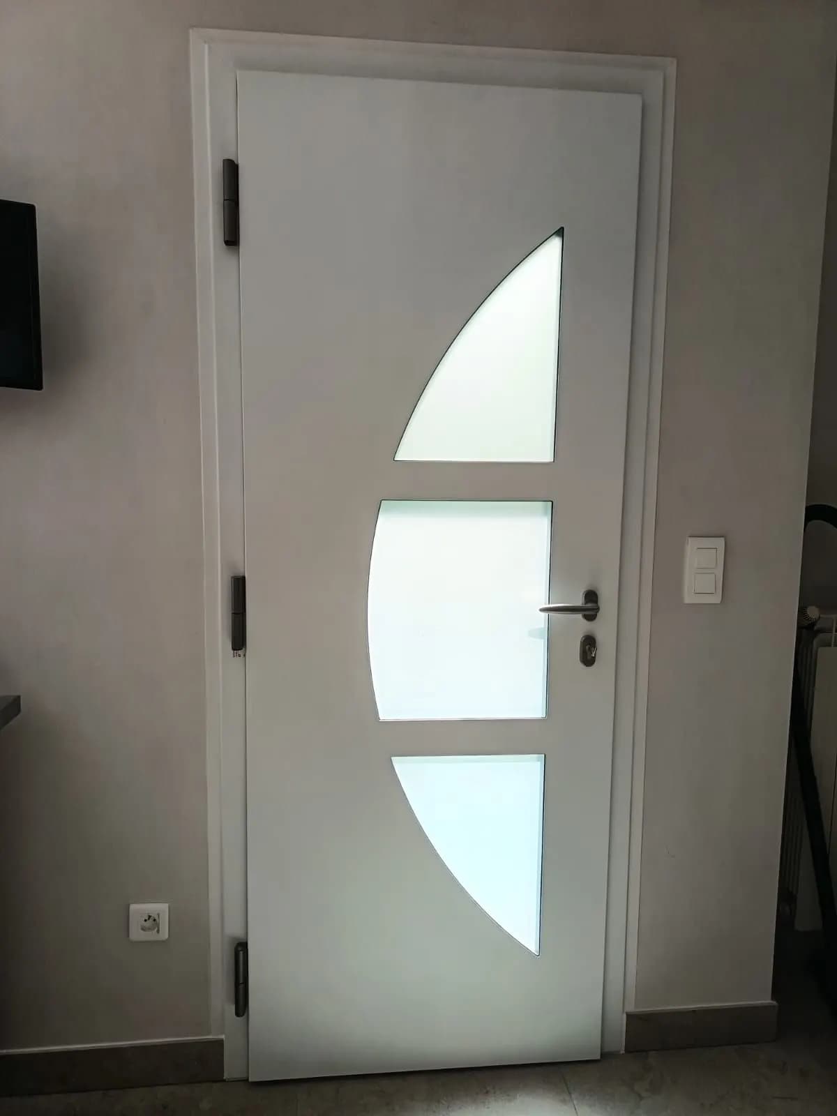 Porte d’entrée blanche vue de l’intérieur, trois vitrages dépolis en arc