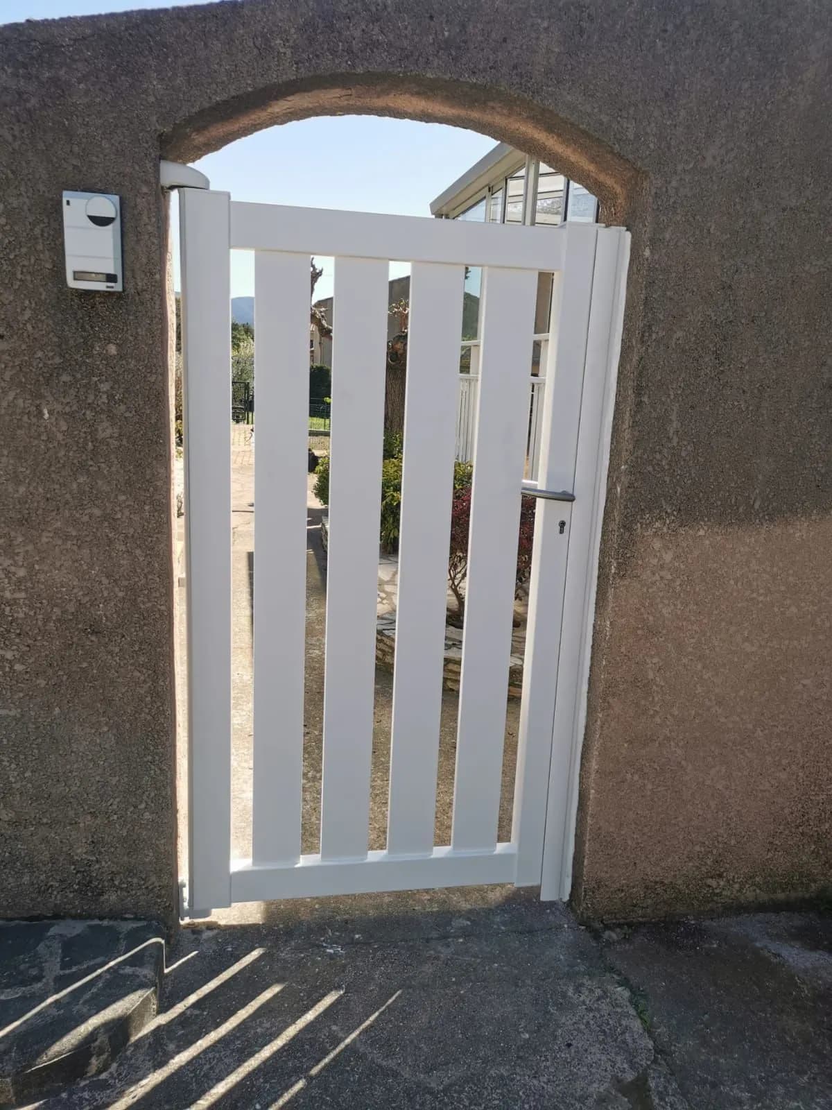 Portillon blanc à lames sous une arche de mur crépi