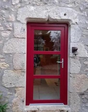 Porte d’entrée rouge vitrée dans un encadrement en pierre