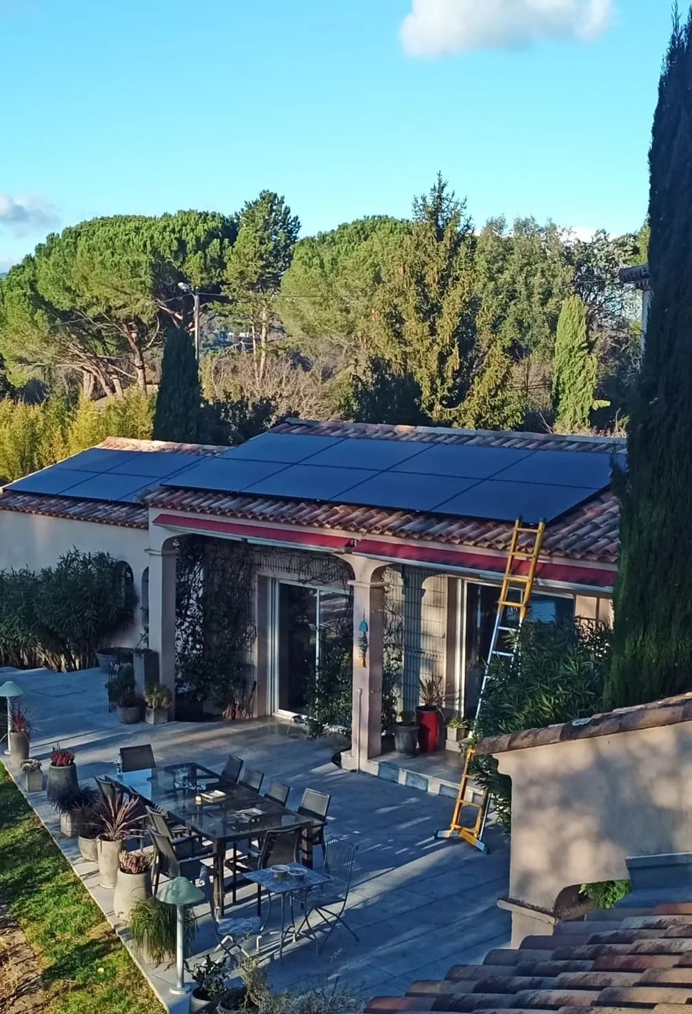 Maison dont deux pans de toiture en tuiles sont couverts de panneaux photovoltaïques noirs, échelle contre la façade