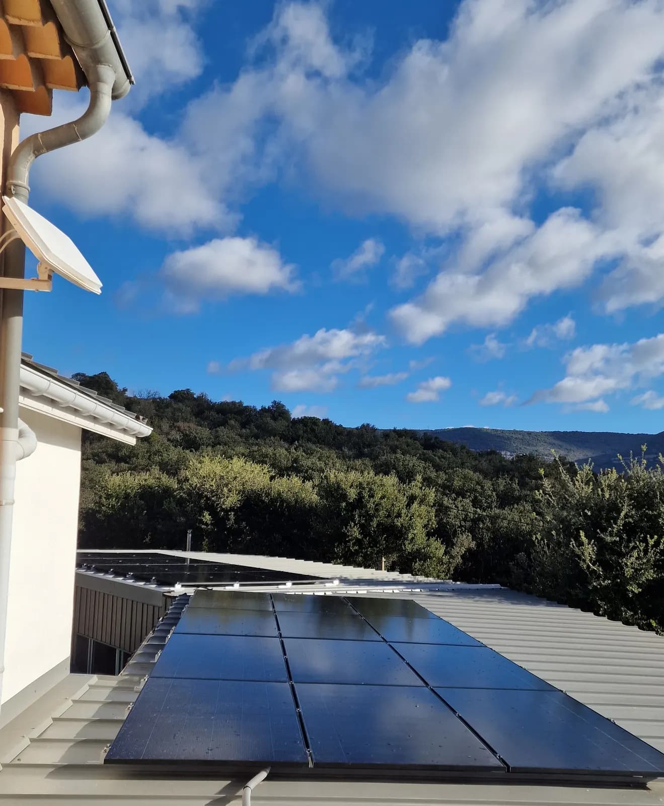 Panneaux photovoltaïques noirs sur un toit en bac acier, collines boisées en fond