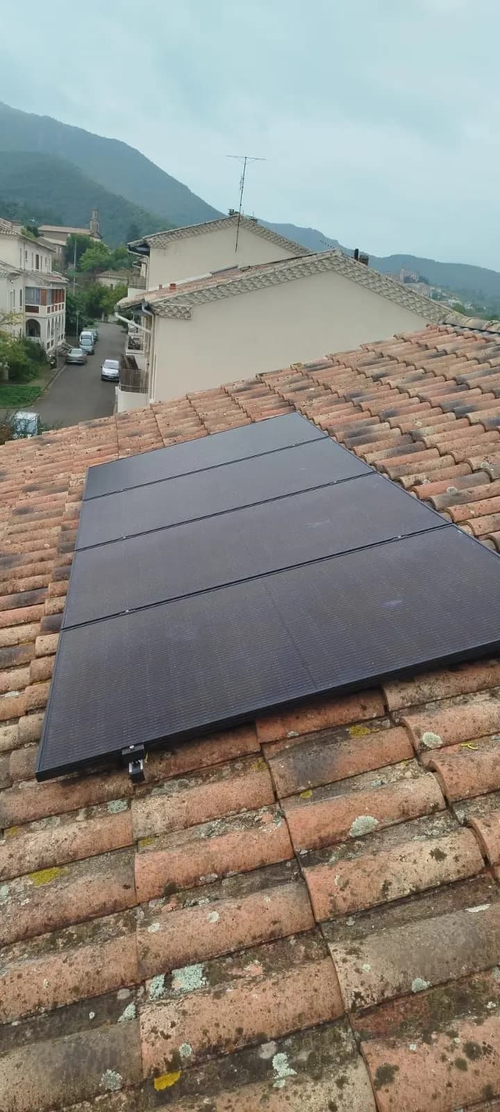 Huit panneaux photovoltaïques sur tuiles, village et montagnes en contrebas