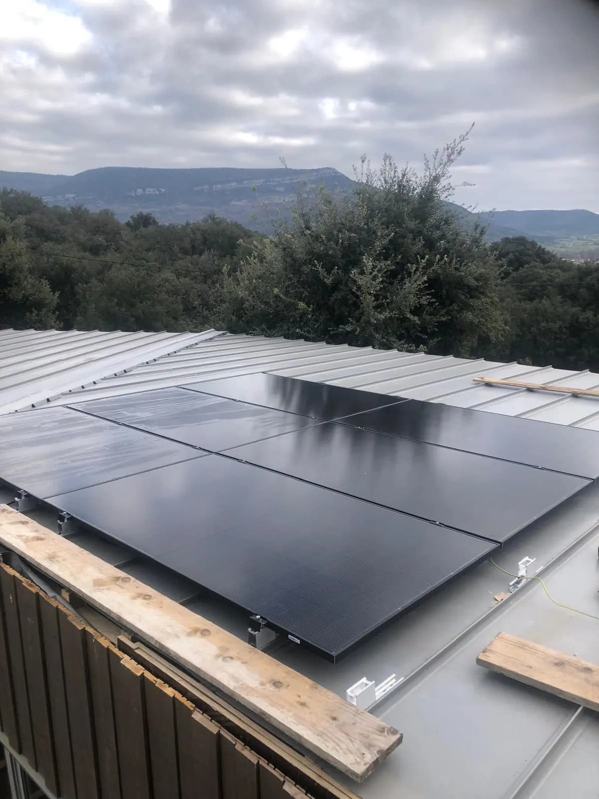 Huit panneaux photovoltaïques sur un toit en bac acier, montagne calcaire en fond