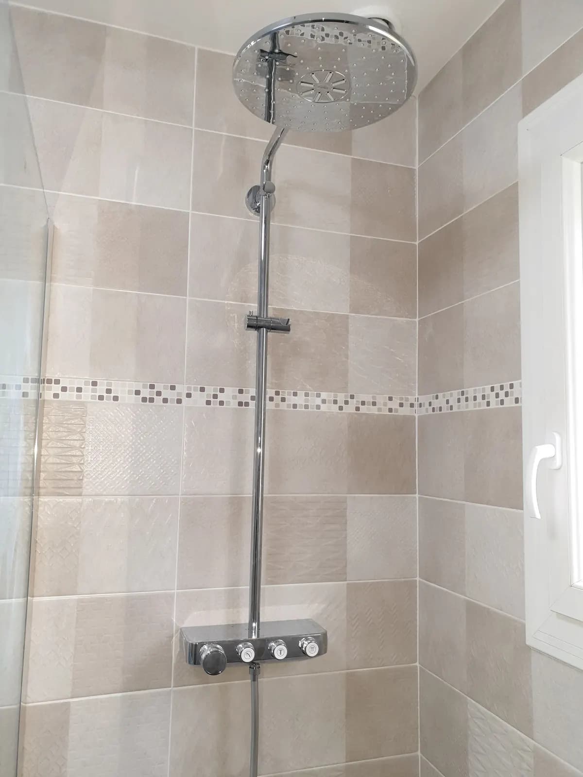 Colonne de douche thermostatique à boutons sur carrelage beige décoré