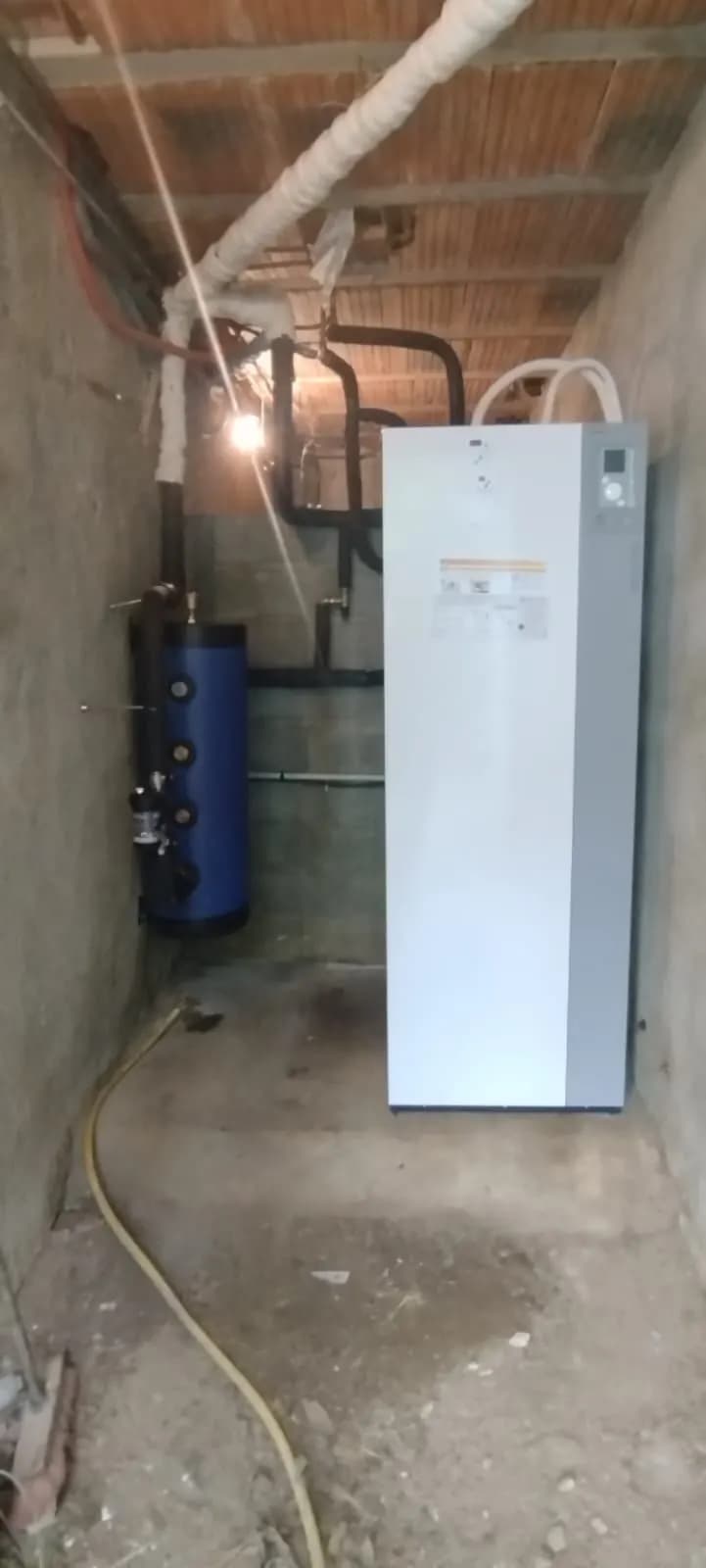 Module intérieur de pompe à chaleur blanc avec ballon tampon bleu dans une cave en brique