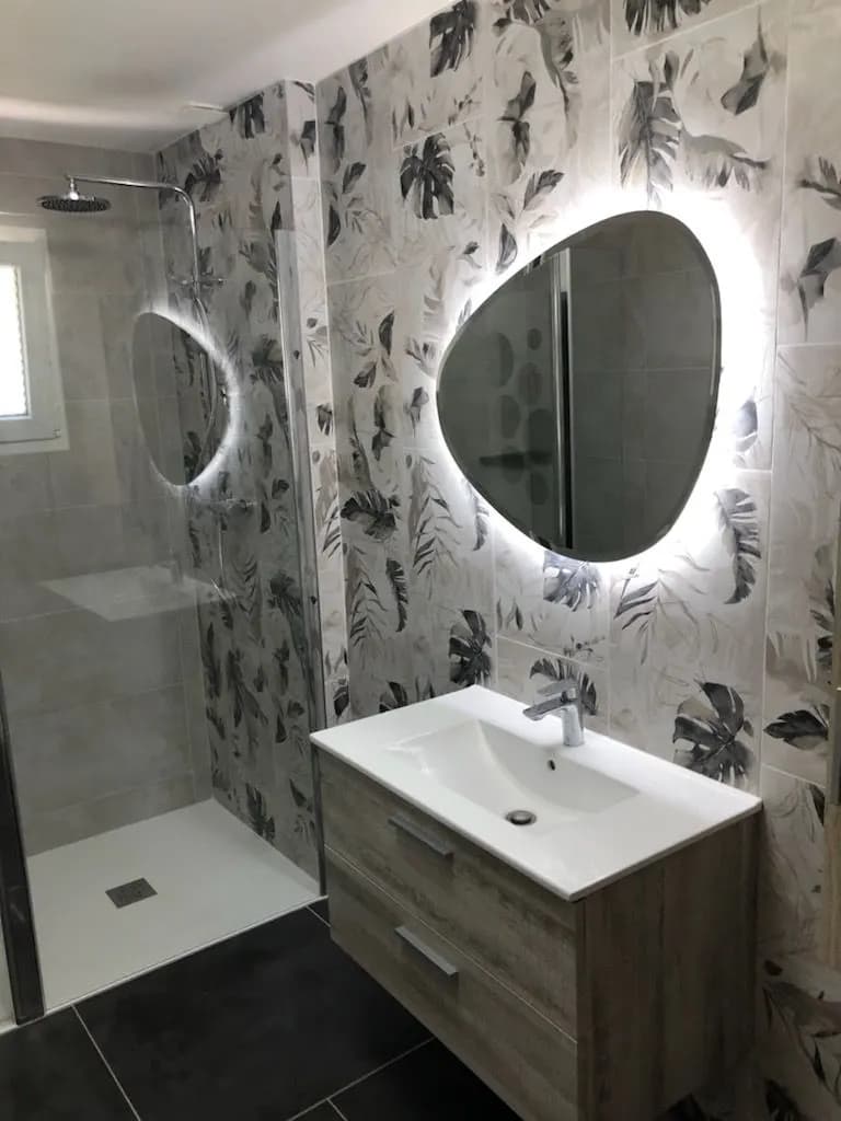 Vasque sur meuble en bois, miroir en forme de galet rétroéclairé et faïence à motif de feuillages