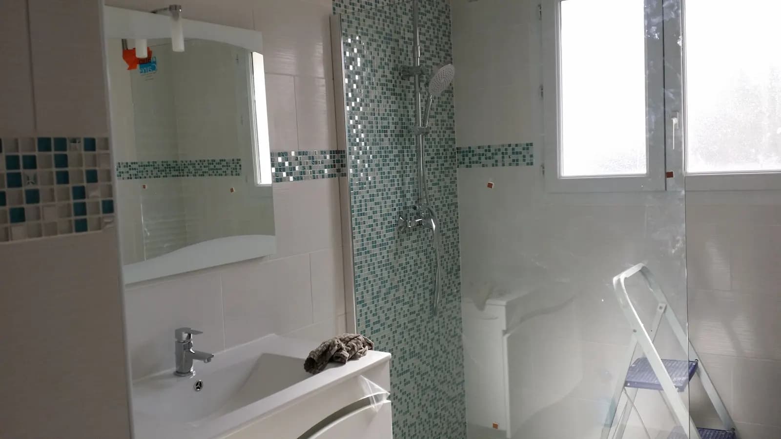 Salle de bain à mosaïque turquoise : douche à l’italienne à paroi de verre et meuble vasque blanc