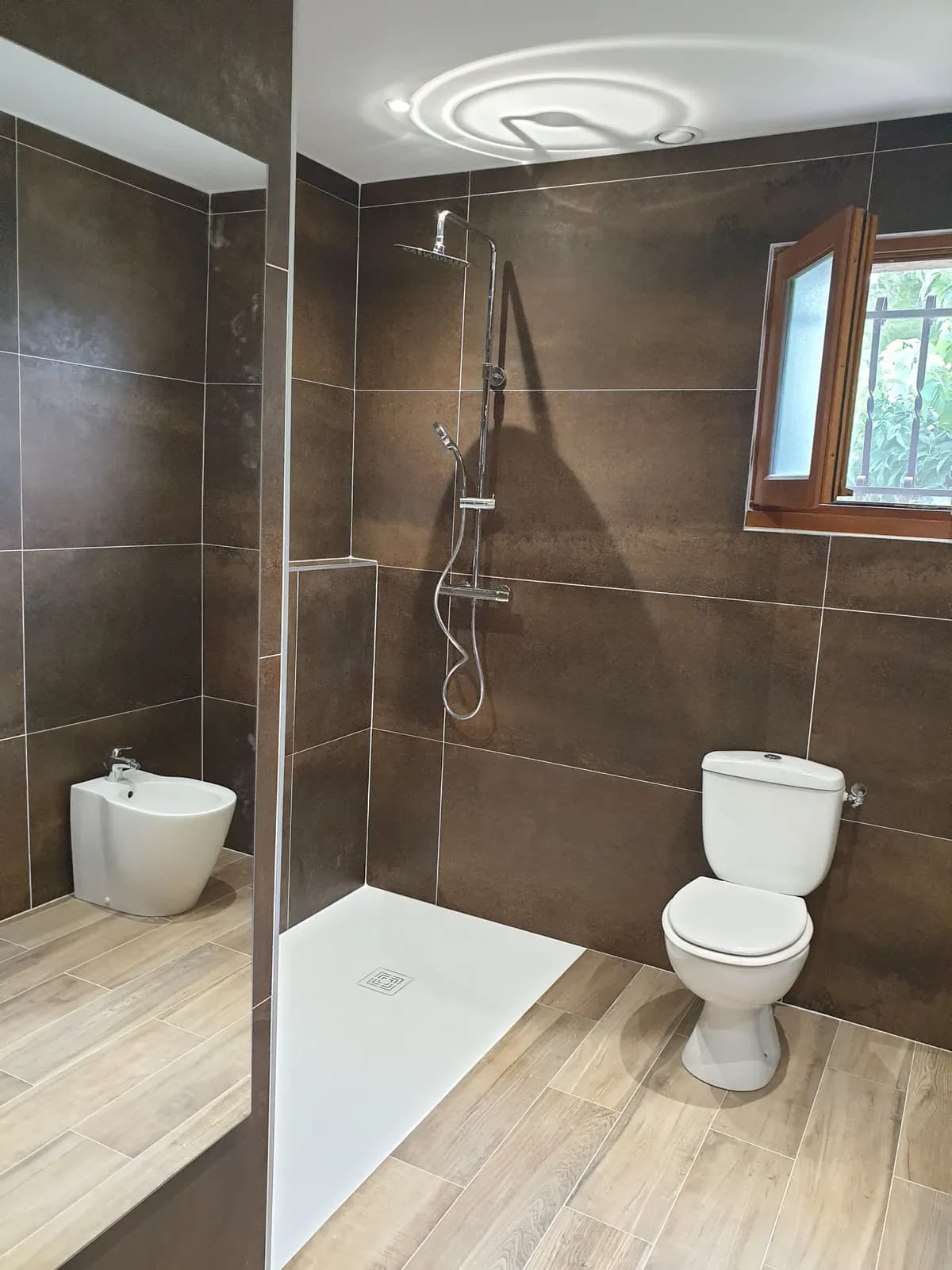 Douche de plain-pied à receveur blanc, WC et bidet dans une salle de bain aux murs bruns