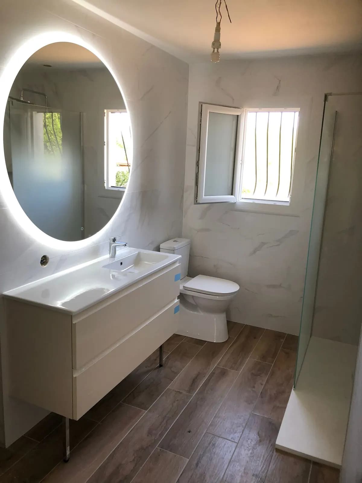 Salle de bain en marbre blanc avec grand miroir rond rétroéclairé et meuble vasque blanc