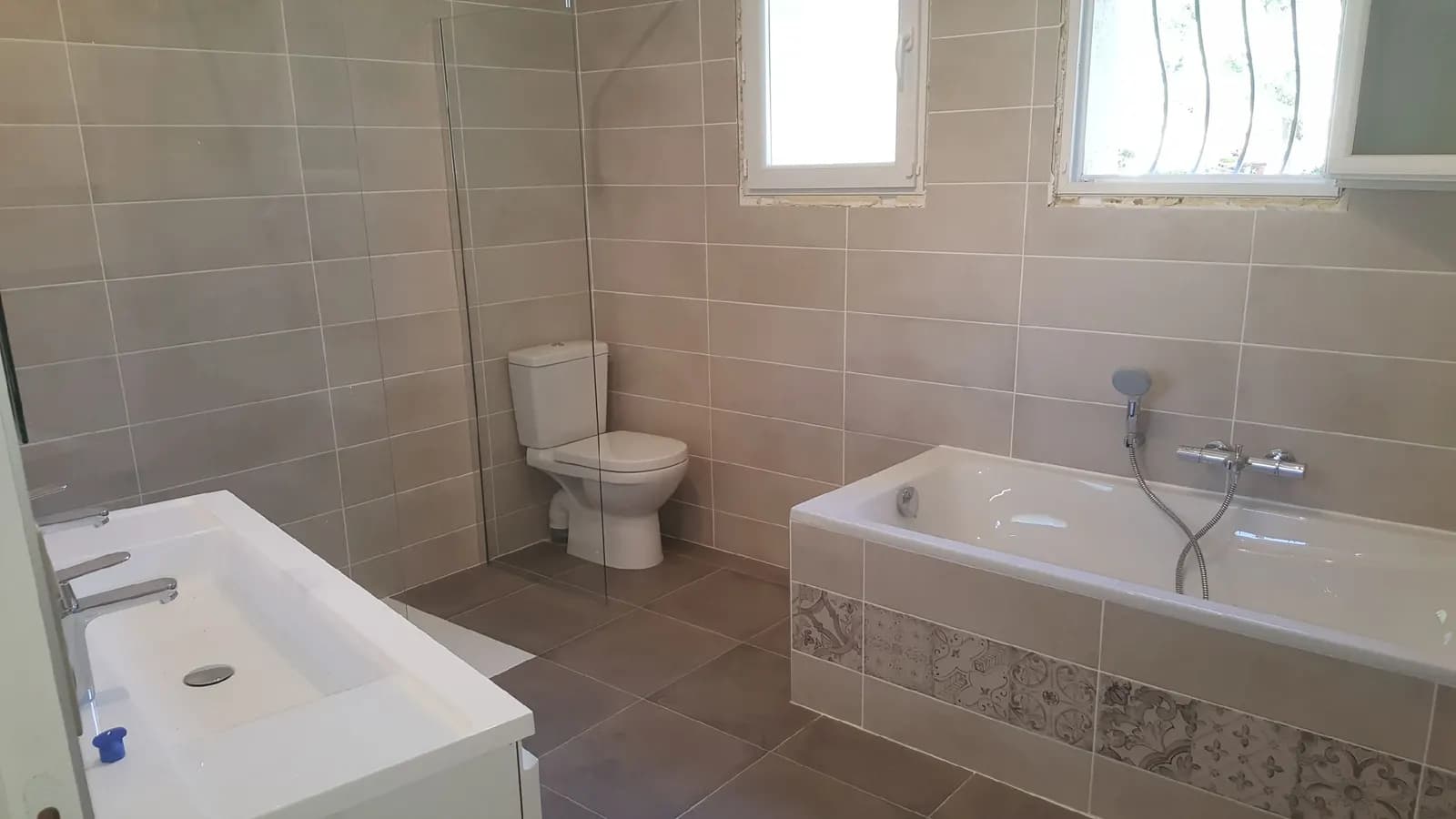 Salle de bain avec baignoire au tablier en carreaux de ciment, paroi de douche et double vasque
