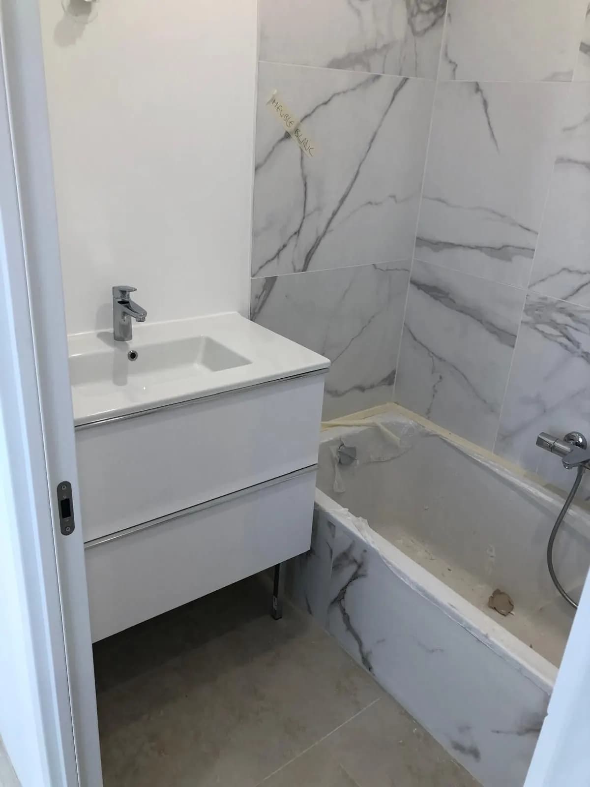 Chantier de salle de bain : marbre blanc, meuble vasque blanc et baignoire sous film