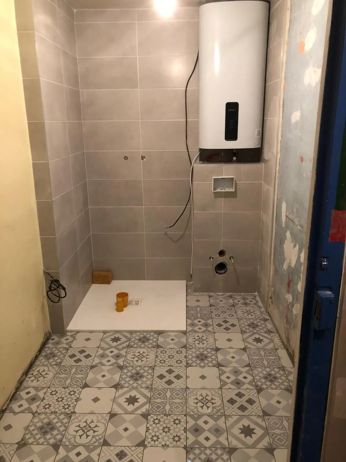 Salle de bain en cours de travaux : faïence grise, sol en carreaux de ciment, attentes de WC suspendu
