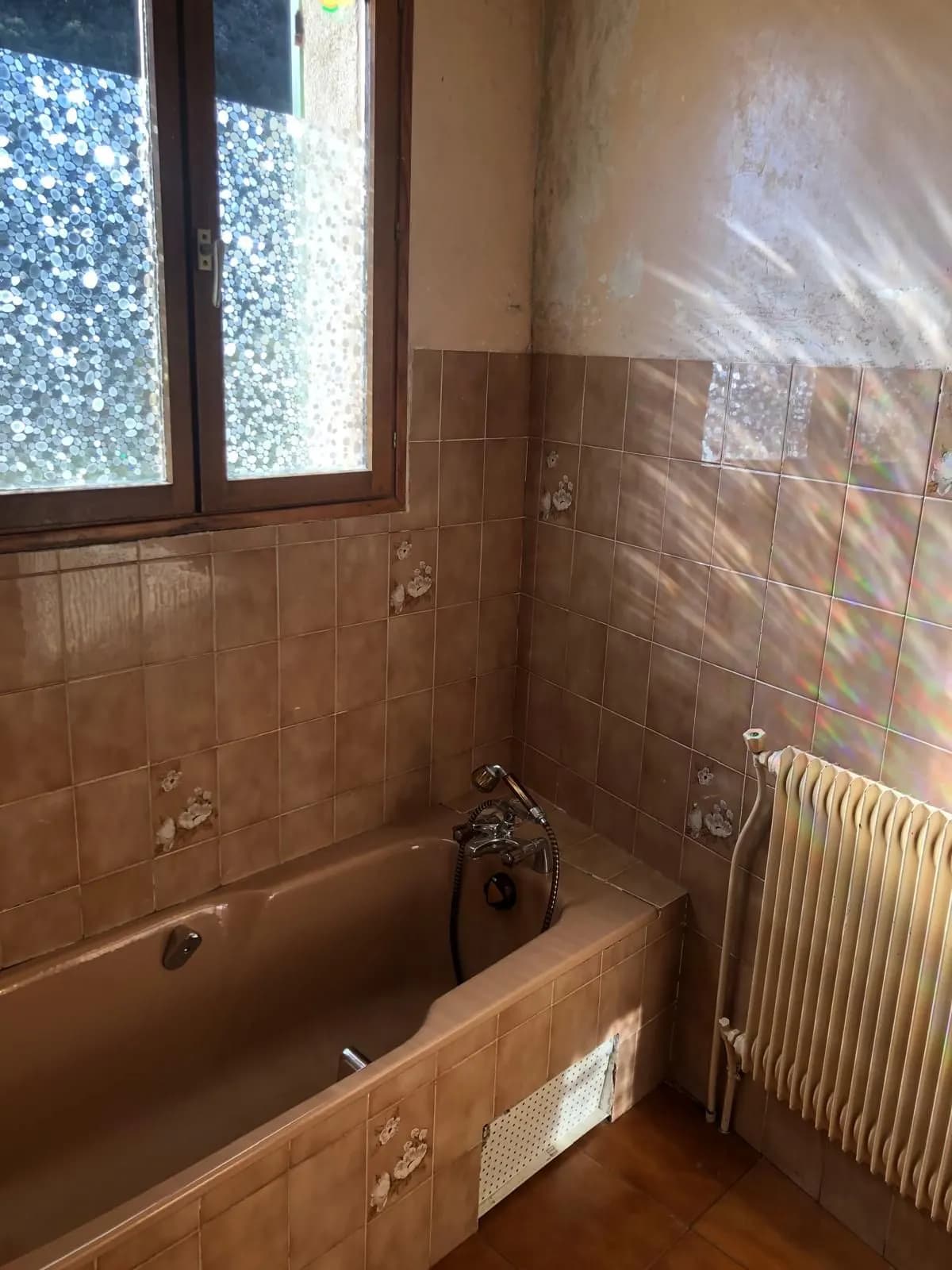 Salle de bain avant travaux : baignoire beige ancienne et faïence à fleurs