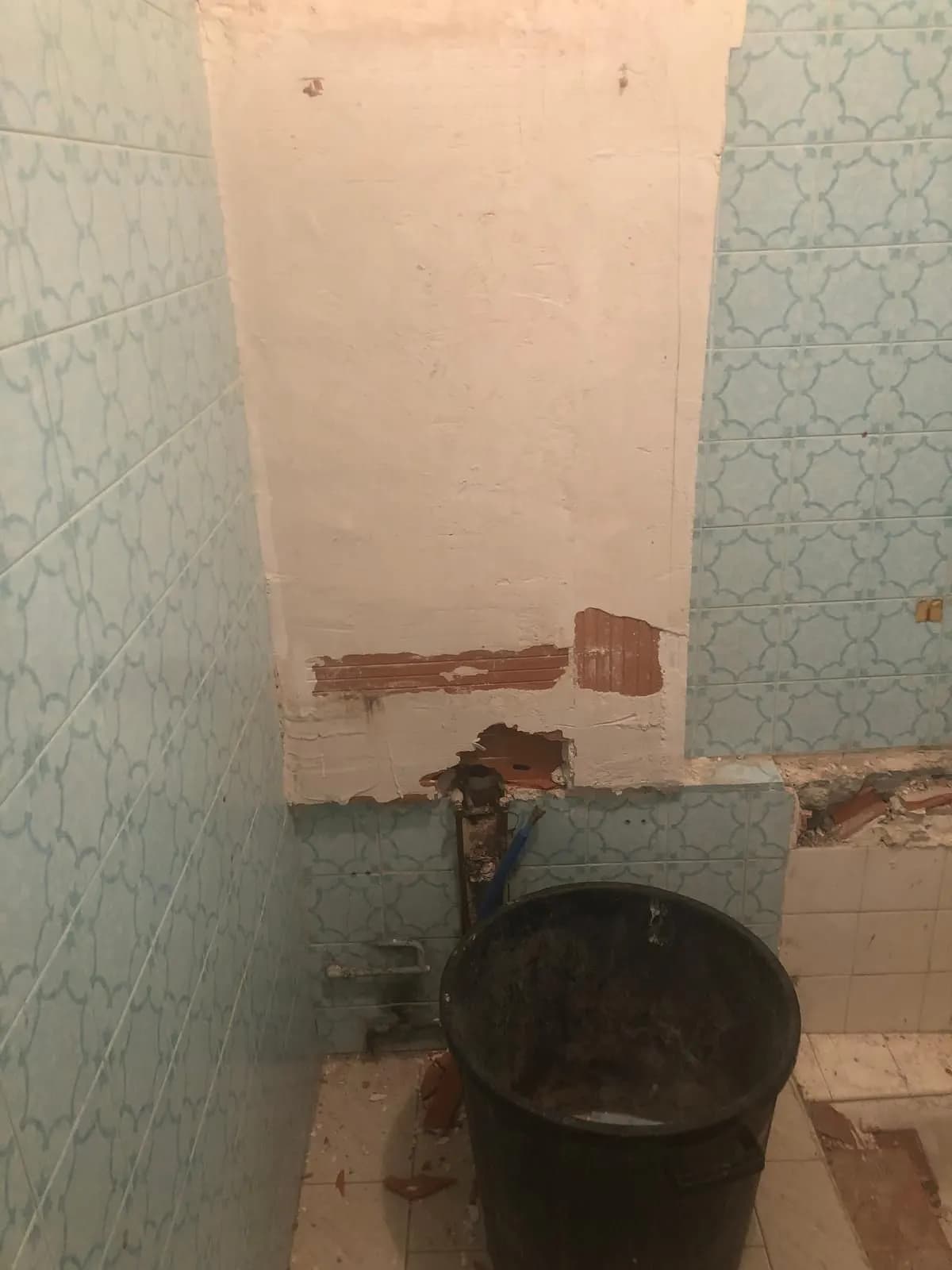 Démolition d’une salle de bain : faïence bleue, mur gratté et tuyaux à nu