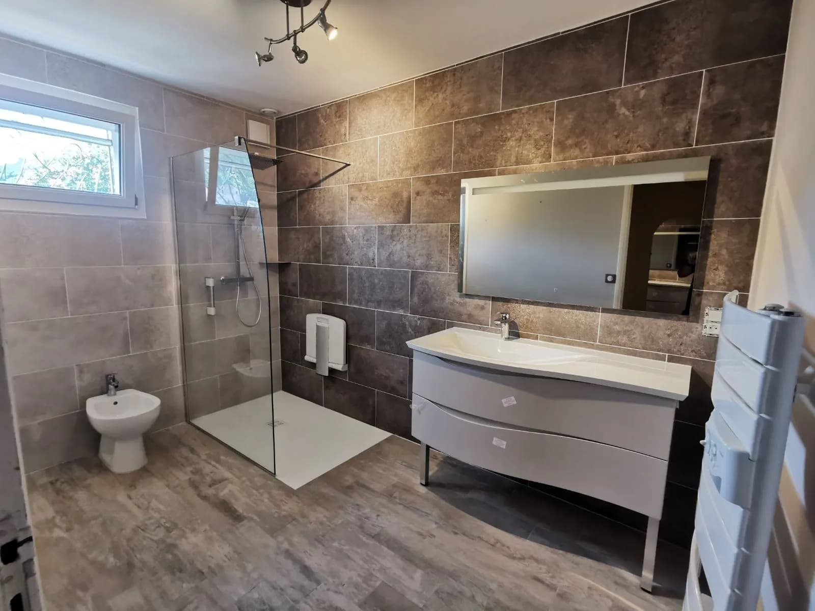 Douche de plain-pied avec siège rabattable et barre d’appui, bidet, meuble vasque et sèche-serviettes